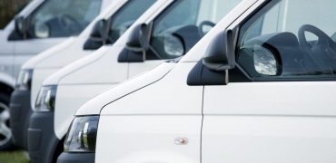 A large group of delivery vans/transporters after work. The first transporter is focused. The vans park in a row. The vans transport/deliver many packages and run removals. The front of the vehicles is shown. The transporters are white. More service vehicles and cars are in my portfolio.