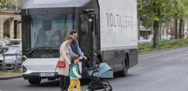 Young family crossing the road in front of a Volta Truck