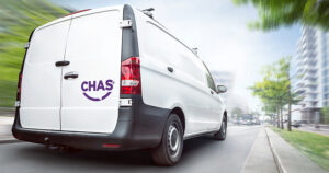 Rear view of a white CHAS van driving in a city. Motion blurred city background with buildings and trees.
