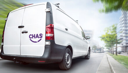 Rear view of a white CHAS van driving in a city. Motion blurred city background with buildings and trees.