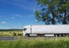 rural landscape with white truck on the road, tall trees against the blue sky with white clouds