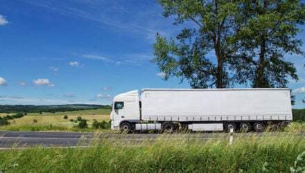 rural landscape with white truck on the road, tall trees against the blue sky with white clouds