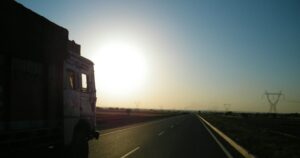 Silhouette of a lorry on the road driving towards the sun