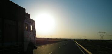 Silhouette of a lorry on the road driving towards the sun