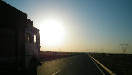 Silhouette of a lorry on the road driving towards the sun