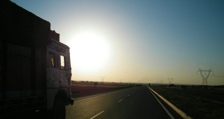 Silhouette of a lorry on the road driving towards the sun